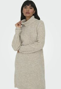 Robe pull en beige avec une texture côtelée, dotée d'un col roulé volumineux et de longues manches. Motif horizontal subtil sur l'ensemble.