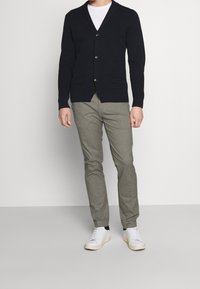 Cárdigan de punto azul marino con escote en V, cierre de botones y dos bolsillos frontales, combinado con pantalones grises claros y zapatillas blancas.