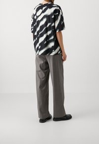 Camiseta de tie-dye en blanco y negro, con mangas cortas, cuello redondo y corte relajado, combinada con pantalones grises holgados y zapatos negros.