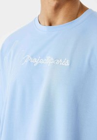 Camiseta de algodón azul claro con texto bordado en el frente "Projectparis" y un diseño de línea simple, cuello redondo y corte relajado.