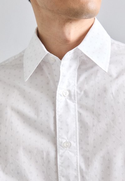 Camisa blanca de botones con un sutil patrón de pequeños triángulos y círculos grises. Cuenta con un cuello clásico y un cierre frontal estándar con botones.