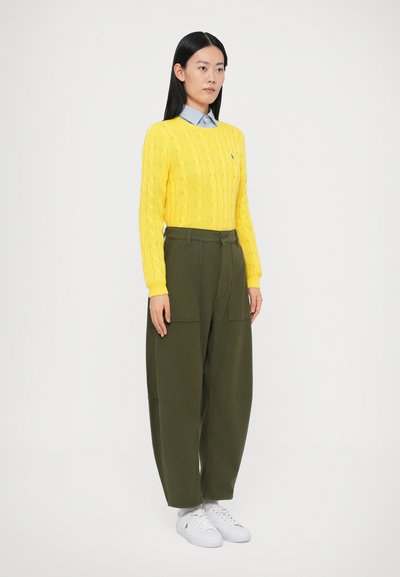 Κίτρινο πλεκτό πουλόβερ με καλώδιο, ανοιχτό μπλε πουκάμισο με γιακά, χακί παντελόνι cargo και λευκά αθλητικά παπούτσια. Απλός σχεδιασμός, υφασμάτινη υφή και τσέπες.