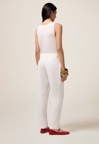 Haut sans manches blanc associé à un pantalon taille haute blanc, avec une finition texturée et un bracelet en or au poignet. Des ballerines rouges complètent le look.