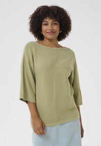 Hellgrüner Strickpullover mit weitem Ausschnitt, 3/4-Ärmeln und subtilen vertikalen Details entlang der Brust; weiche Textur und lockere Passform.