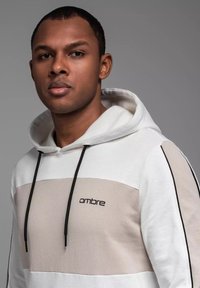 Sudadera blanca y beige con un diseño en el panel frontal, cordones y logo "ombre". Confeccionada en un tejido suave con acentos laterales en contraste.