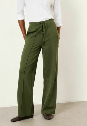 Green wide-leg pants with a drawstring waist and silver eyelets, featuring vertical seams and a smooth, textured fabric.