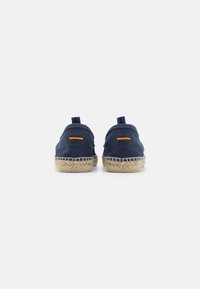 Espadrilles de lona azul marino con suela de yute, con un acabado texturizado y un pequeño acento naranja, diseñados con un perfil bajo y una lengüeta en la parte posterior.