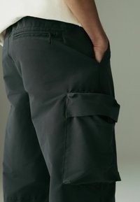 Pantaloni cargo negri, cu un buzunar lateral, textura netedă și detalii cu șnur la talie, concepuți pentru funcționalitate și confort.