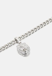 Bracelet en chaîne argentée présentant un pendentif en forme de tête de lion avec des traits faciaux détaillés et une crinière texturée. Conception de maillons robuste.