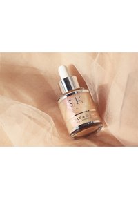 Bottiglia di vetro con pipetta e tappo argento, contenente un siero beige chiaro etichettato "GET UP & GLOW", posizionato su uno sfondo di morbido tessuto pesco.