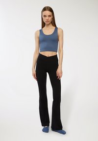 Top corto azzurro abbinato a pantaloni neri a campana. Il top presenta un scollatura arrotondata; i pantaloni hanno una vita alta e un design semplice.