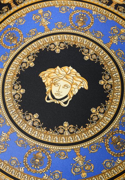 Okrogla svilena ruta s črnim in modrim ozadjem ter zlato okrašenimi vzorci. Osrednji motiv je zlata glava Meduze.