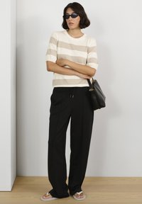 Pulover z rjavimi in bež črtami, kombiniran s črnimi ohlapnimi hlačami. Dodatki vključujejo majhno črno torbico in temna sončna očala.