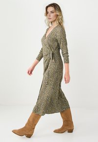 Bottes en daim marron montant jusqu'au genou, associées à une longue robe portefeuille à motifs, avec un col en V, des manches trois-quarts et un ourlet fluide.