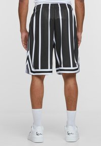 Svarta sportshorts med vita vertikala ränder, elastisk midja och sidoöppningar vid nederkant. Tillverkade av lättviktsmaterial.