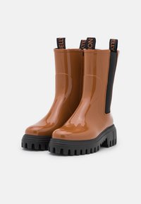 Bottes de cheville en caoutchouc marron avec une finition brillante, un talon carré et des panneaux latéraux élastiques noirs. Comprend une tirette avec un accent du nom de la marque.