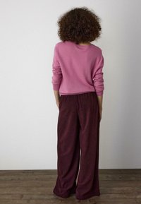 Ružový sveter s dlhými rukávmi v kombinácii s vínovými širokými nohavicami z kordurovej látky s textúrovaným povrchom a elastickým pásom.