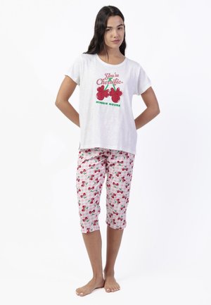 Mujer vistiendo una camiseta blanca de manga corta con cerezas rojas y texto, combinada con pantalones cortos de cuadros rosa y blanco con estampados de cerezas.