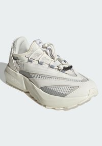 Biele tenisky s kombináciou hladkých a textúrovaných materiálov, s priedušnými panelmi, masívnou podrážkou a reflexnými akcentmi na šnúrkach.