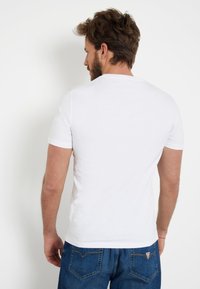 Balta trumpa rankovėmis marškinėliai su apvalia iškirpte, pagaminti iš minkštos medvilnės, rodantys paprastą dizainą be raštų ar grafikų.