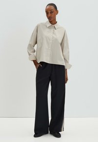 Lightly striped beige button-up shirt with a relaxed fit paired with black wide-leg pants featuring a side stripe detail.