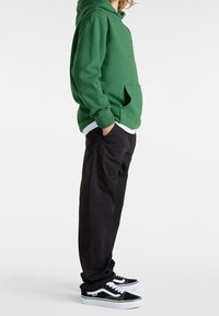 Groene hoodie met een voorzak, gecombineerd met zwarte broek en zwart-witte sneakers. Heeft een eenvoudig, casual ontwerp.