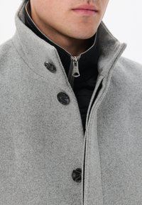 Cappotto grigio in misto lana con colletto alto, fodera con zip nera e bottoni neri per la chiusura. Texture morbida con vestibilità strutturata.