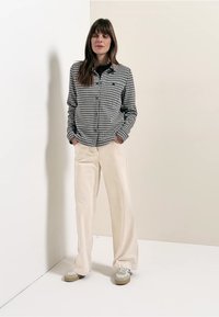 Svartvit rutig skjorta med knappar tillsammans med krämfärgade vida byxor och ljusa sneakers, mot en neutral bakgrund.