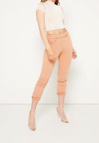Meruňkové tepláky s elastickým pasem a manžetami, doplněné o přiléhavý béžový crop top. Hladká tkanina s ležérním designem.