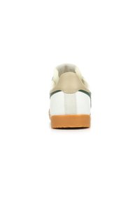 Vista trasera de una zapatilla que presenta un cuerpo de cuero blanco, acentos beige en el talón, una franja verde y una suela de goma marrón.