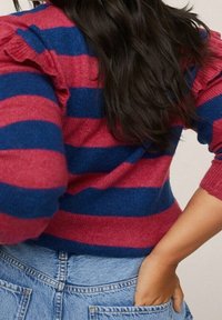 Rot und blau gestreifter Pullover mit Rüsche an den Schultern; mittlere Stricktextur; kombiniert mit hochtaillierten Denim-Shorts.