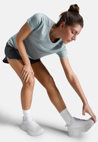 Světle modré sportovní tričko s krátkým rukávem a kulatým výstřihem, spárované s černými šortkami. Na nohou bílé, polstrované sportovní boty a bílé ponožky.