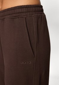 Brown sweatpants with a ribbed waistband, featuring side pockets and the word "BORG" embroidered in a matching brown tone. Soft material.