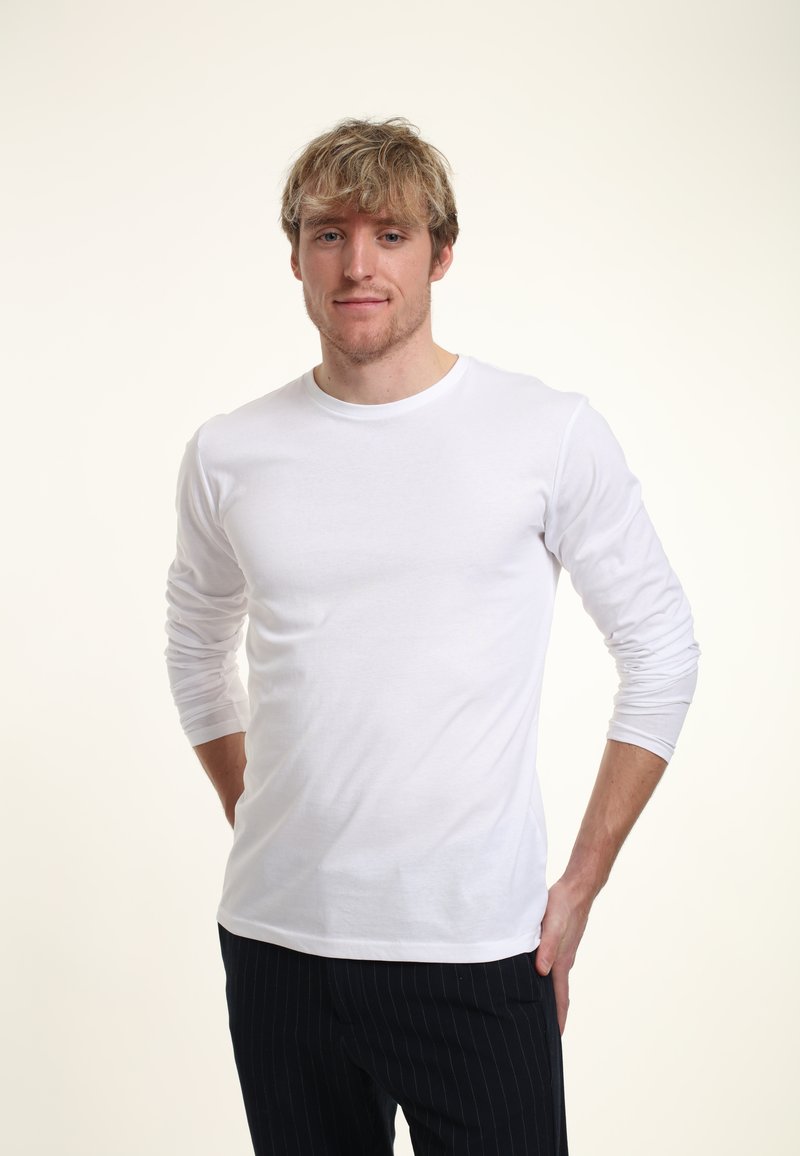 Bílé tričko s dlouhým rukávem a kulatým výstřihem, přiléhavého střihu a hladké textury, doplněné pruhovanými kalhotami.