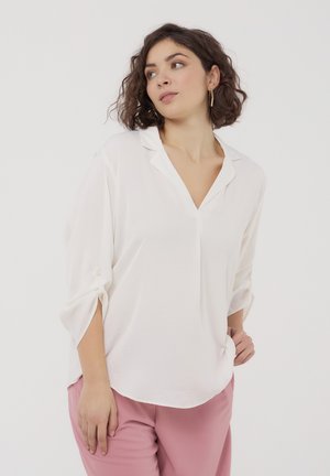 Blusa bianca con scollatura a V e maniche a tre quarti, con dettagli di bottoni sulle maniche, abbinata a pantaloni rosa. Texture liscia.