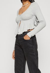 Camiseta gris de manga larga con cierre de botones, detalles de encaje y dobladillo acampanado, combinada con jeans de mezclilla negra de tiro alto.