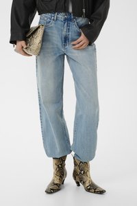Personne portant un jean large bleu clair, une veste noire, tenant une pochette en cuir de serpent et portant des bottines à talons en cuir de serpent assorties.