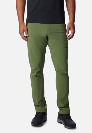 Herren Outdoor-Hosen in Grün aus leichtem Stoff; verfügen über dehnbares Material, schmalen Schnitt und seitliche Taschen. Getragen mit schwarzen Schuhen.