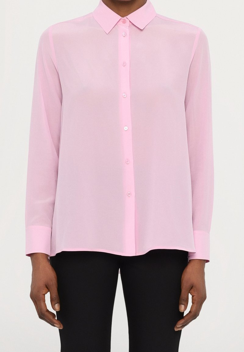 Chemisier en voile rose clair avec un col classique, des manches longues et une fermeture à boutons. Présente des poignets roses unis et un ourlet droit.