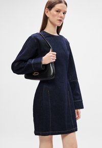 Τζιν φόρεμα σε σκούρο μπλε χρώμα με μακριά μανίκια και άνετη εφαρμογή, με αντίθετη πορτοκαλί ραφή. Μαύρη τσάντα χειρός με χρυσές λεπτομέρειες.