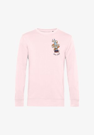 Lyserød langærmet skjorte med et håndmotiv i tatoveringsstil, der holder et banner med teksten "FRIDA", og "Frida Kahlo" skrevet nedenunder.