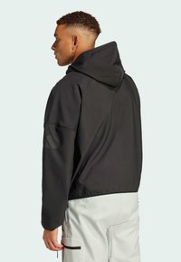 Black hoodie with a relaxed fit, featuring a drawstring hood and subtle branding detail on the left sleeve. Smooth, lightweight fabric.