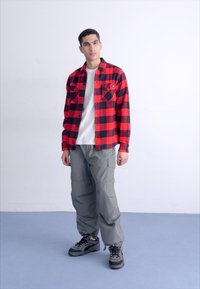 Rød og sort ternet flannel-skjorte med knaplukket brystlomme, parret med grå cargobukser og sorte sneakers. Enkel, afslappet design.