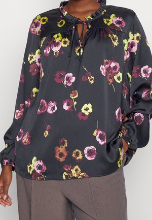 Blouse noire à motif floral coloré ; présente un col orné de volants et un détail noué, des manches longues avec des poignets élastiques, et une texture lisse.