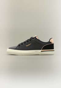 Μαύρο αθλητικό παπούτσι με λείο συνθετικό σώμα, κρέμ λαστιχένια σόλα και μεταλλικά ροζ χρυσά στοιχεία στη φτέρνα και την πλαϊνή πλευρά. Φέρει το όνομα της μάρκας.