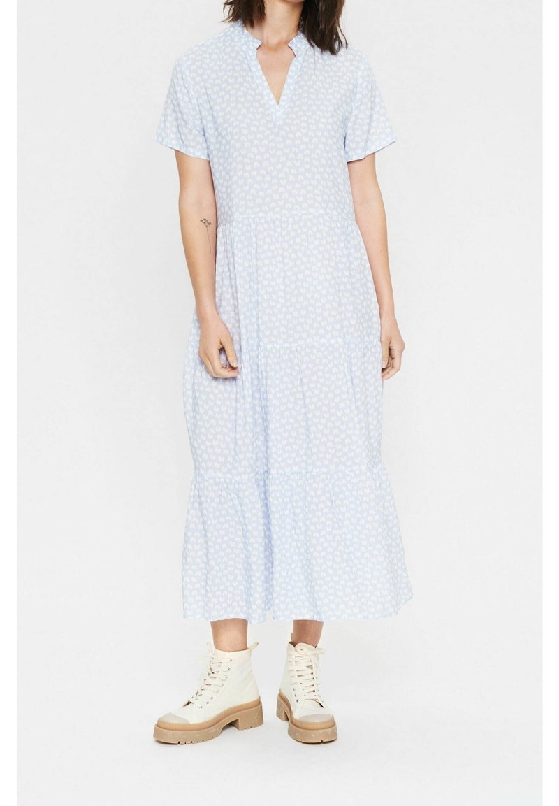Hellblaues Kleid mit kurzen Ärmeln, V-Ausschnitt, gestuftem Design und weißem Herzmuster, aus weichem Stoff. Getragen mit cremefarbenen Schnürstiefeln.