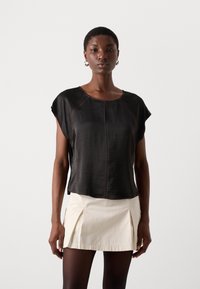 Schwarzes T-Shirt mit kurzen Ärmeln und leicht strukturiertem Finish, mit kontrastierendem braunem Nähten und lässiger Passform, kombiniert mit einem cremefarbenen Rock.