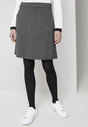 Czarna i biała spódnica w jodełkę o rozkloszowanym kroju, zestawiona z czarnymi rajstopami i białymi trampkami. Gładka faktura i usztywniony pas.