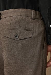 Brown striped trousers with a textured fabric, featuring a back pocket with a button closure and a classic waistband design.