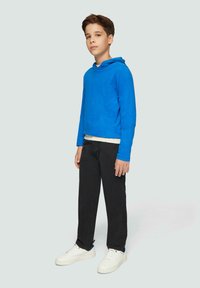 Hoodie bleu à manches longues avec une poche kangourou à l'avant, associé à un pantalon noir et des baskets blanches avec des accents marine. Texture lisse.